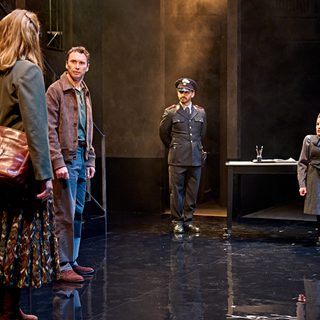 A production image from ‘Don’t Look Now.’ Laura and John stand on one side of the room, whilst a policeman and the Clerk stand on the other. Everyone is looking towards Laura, who has her back turned to the camera. John has a fearful expression on his face.