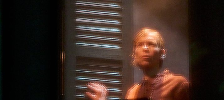 A production image from ‘Don’t Look Now.’ One of the sisters stands at the top of some stairs in the middle of a doorway, looking out towards the stage. The image has a blurred effect to it.