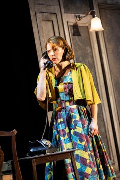 A woman standing as she holds an old-fashioned phone to her ear, frowning.
