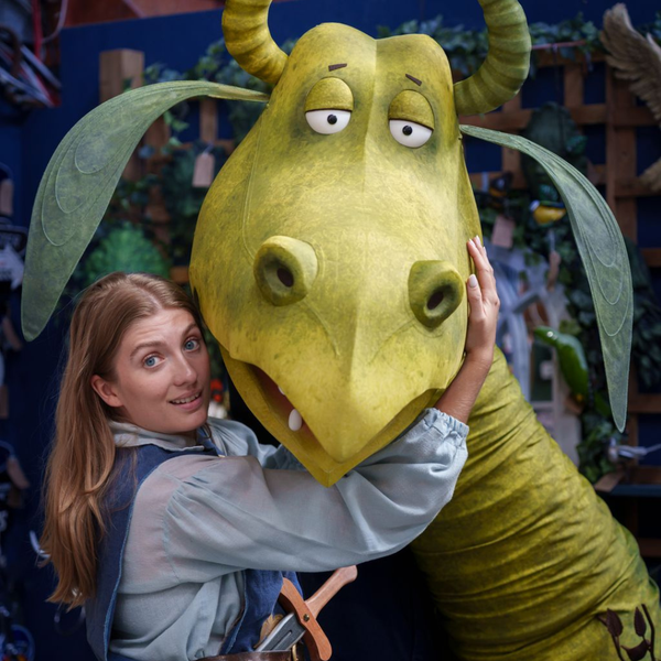 A woman dressed in medieval costume holding a large dragon puppet of Charlie Stinky Socks.