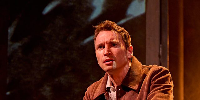 A production image from ‘Don’t Look Now.’ John stands at the top of some stairs, resting his hands on the metal railings in front of him. He looks confused at something he has seen.