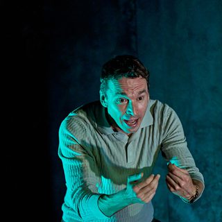 A production image from ‘Don’t Look Now.’ John is shouting, with a terrified look on his face, and is throwing his arms out in front of him. He is lit from the left in blue lighting.