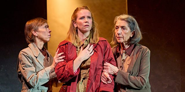 A production image from ‘Don’t Look Now.’ Laura stands in the middle of the two sisters, who are each clutching onto one of Laura’s arms. Laura holds one hand to her chest and looks out into the distance, with a look of concern on her face.