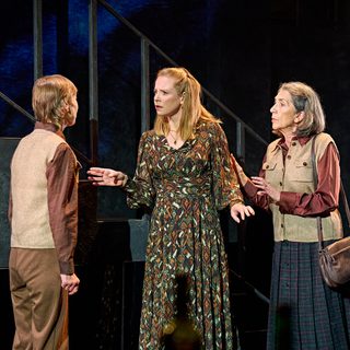 A production image from ‘Don’t Look Now.’ Laura is stood in the middle of the two sisters, who are telling her some information. She looks slightly shocked by what has been told to her. One of the sisters, stood behind Laura, puts her arm on Laura’s back, perhaps trying to comfort her.