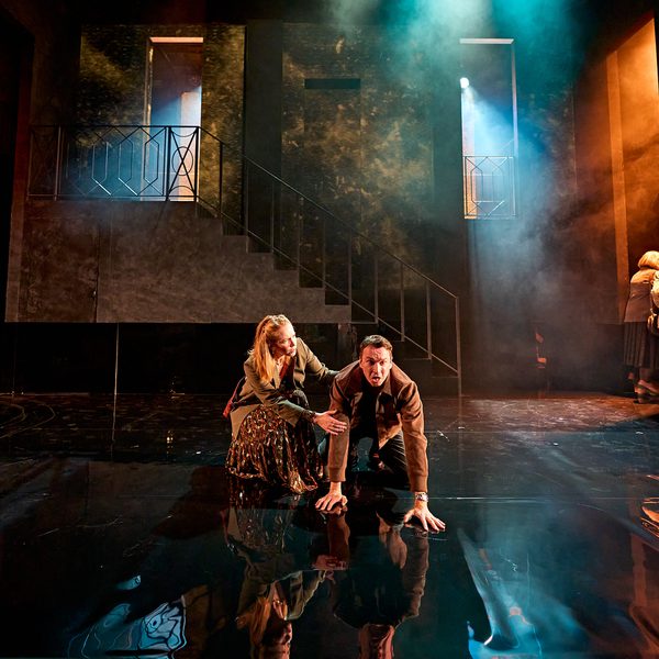 A production image from ‘Don’t Look Now.’ Laura kneels beside John, who is on his hands and knees in the centre of the stage. Laura looks to be comforting John, who has an angry/distraught expression on his face.