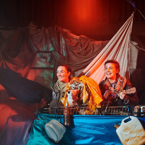 The cast of Stories in the Dust performing on stage, adventuring in a boat made of blankets.