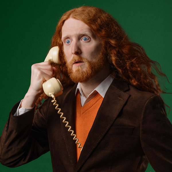 Alasdair Beckett-King, a caucasian man with long way ginger hair, holding a phone to his ear with a shocked expression on his face.