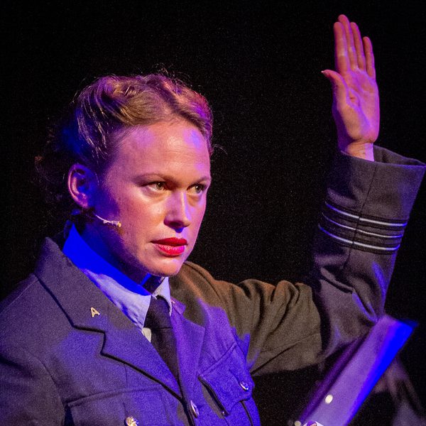 Louise Jordan dressed in a WWII-era uniform, holding a book with her hand raised.