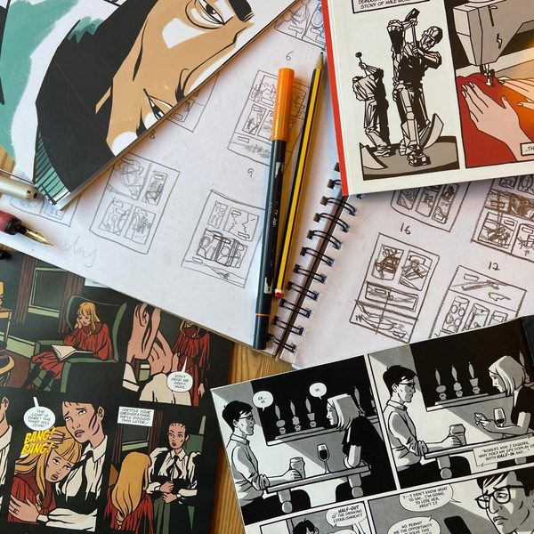 Comic books, storyboard sketches, and drawing pens spread across a table, showing the process of creating illustrated stories and graphic novels.