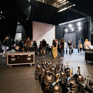 Creative Careers Day participants learning about equipment on a theatre stage, with lighting fixtures, flight cases, and a large projection screen visible.