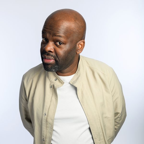 Comedian Daliso Chaponda looking sceptically at camera with his hands behind his back against a white background.
