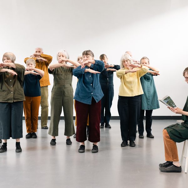 A group of older people in colourful clothes with their arms raised in a dance.