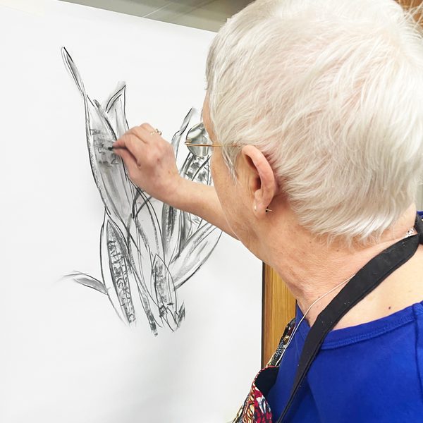 A woman drawing a plant with charcoal on a white sheet of paper.
