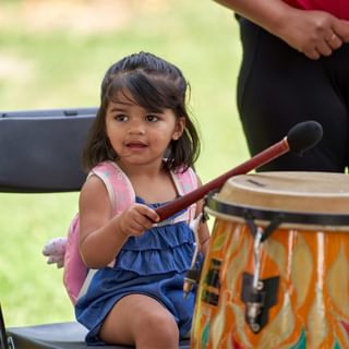 A young girl sat on a chair with a beater banging a drum