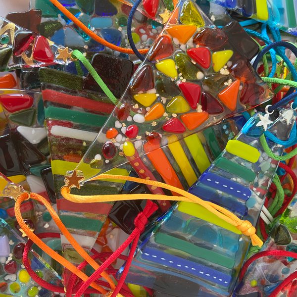 A pile of colourful, fused glass Christmas tree shaped ornaments.