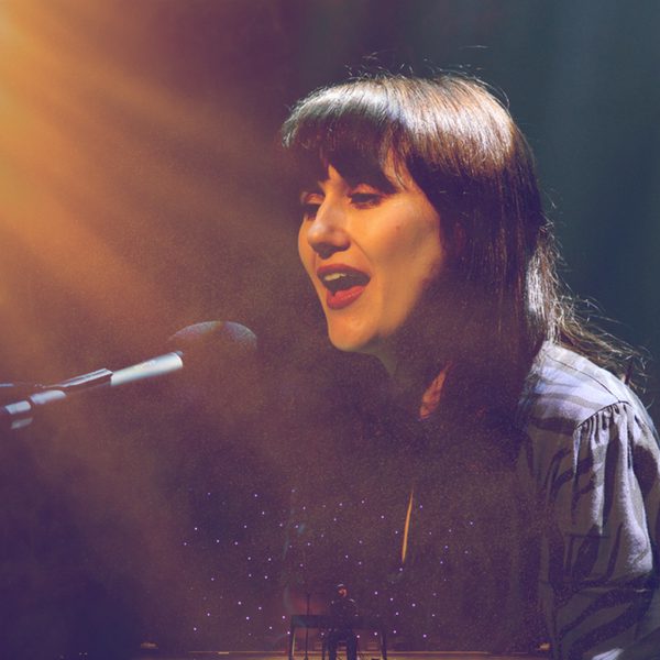 A woman with dark hair singing into a microphone on stage.