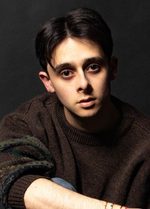 A photo of East is East cast member Rohan Macleod. He has short hair and is wearing a jumper with one sleeve pushed up to the elbow.