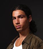 A headshot of East is East cast member Zaki Ali. He has long hair tied back and is wearing an open jacket over a t-shirt.