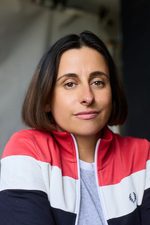 A headshot of East is East cast member Zoe Iqbal. She has chin-length hair and is wearing a stiped jacket.