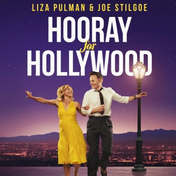 Liza Pulman and Joe Stilgoe performers dressed in vintage-inspired attire walk and dance across a stage-like surface beside a glowing street lamp. Liza wears a bright yellow dress and Joe a white shirt with dark trousers and a loosened tie. Distant mountains and city lights form the background, creating a classic Hollywood atmosphere. Text reads "Liza Pulman and Joe Stilgoe, Hooray for Hollywood"