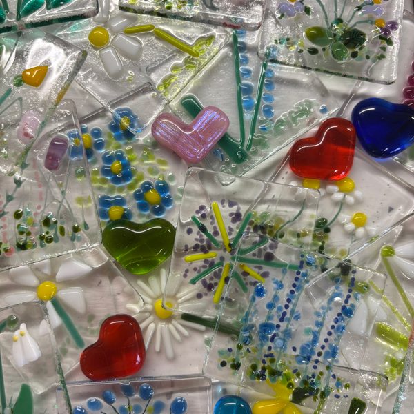 A photo of several fused glass sheets with hearts and flowers embedded into them.