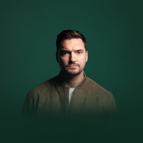Studio portrait of a person with short dark hair wearing a brown zip-up jacket over a light top, facing the camera against a dark green gradient background