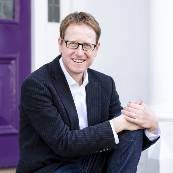 Author Jonathan Freedland sitting in front of an outside door, facing the camera.