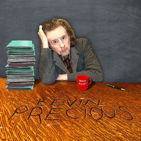 Comedian Kevin Precious in a grey suit leaning over a wooden table, with a stack of books and a red mug superimposed next to him. Text: Kevin Precious.