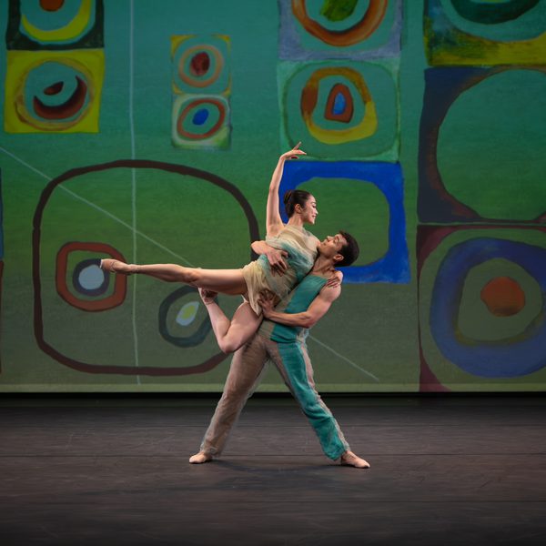 Two London City Ballet dancers in front of a colourful backdrop: a man raises a woman in a lift.