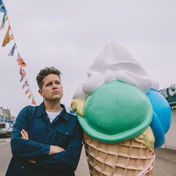 Poet Luke Wright posing on a seaside street next to a large statue of an ice cream cone.