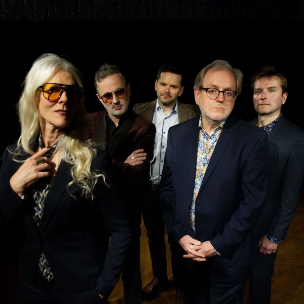 All five members of Moscow Drug Club (Left to Right: A blond woman and four white men) standing in a row in suits and sunglasses.