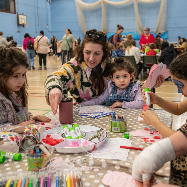 Several young children and adults sat around a colourful table, taking part in various arts and crafts.