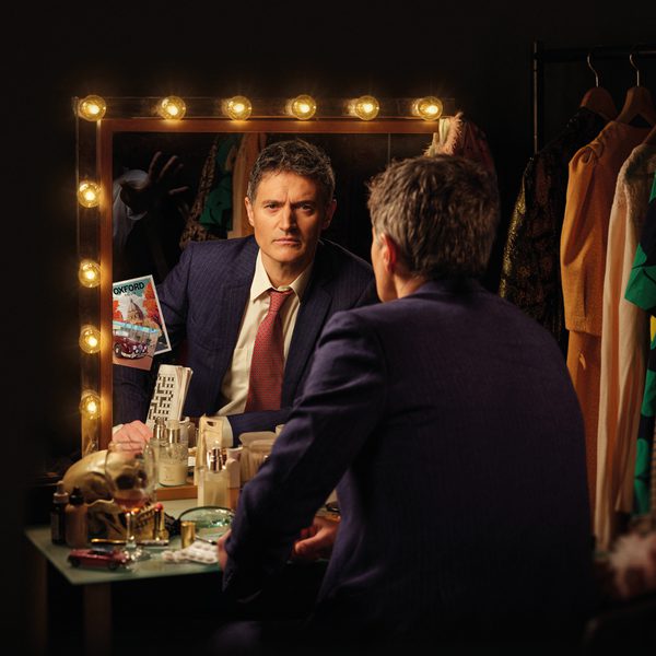 Tom Chambers as Inspector Morse sitting down and looking at the camera through a dressing room mirror.