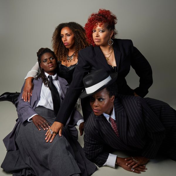 Four women in suits laying in various positions on top of one another against a grey background