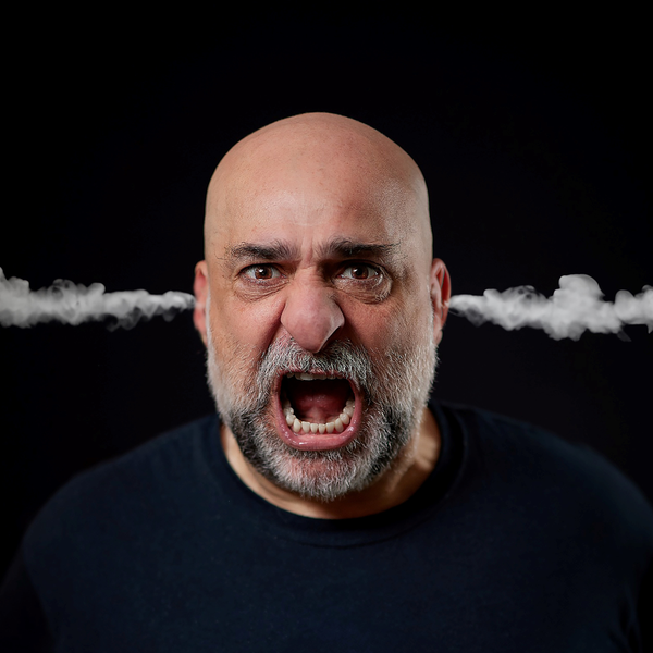 A photo of comedian Omid Djalili against a black background with smoke blowing out of his ears.