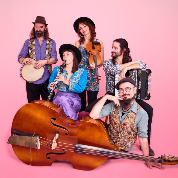 Studio portrait of five people posed with acoustic instruments against a pink background