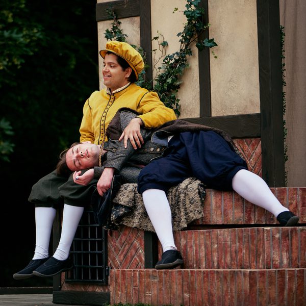Two actors dressed in Shakespearean garb, one with his head on the other's lap.