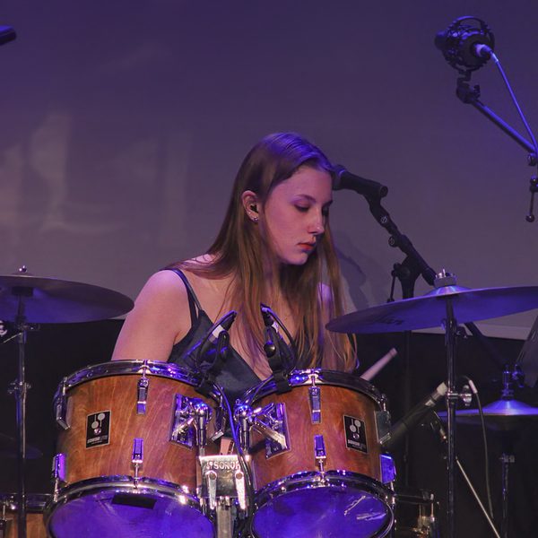 A teenage girl sitting behind a drumkit, playing the drums.