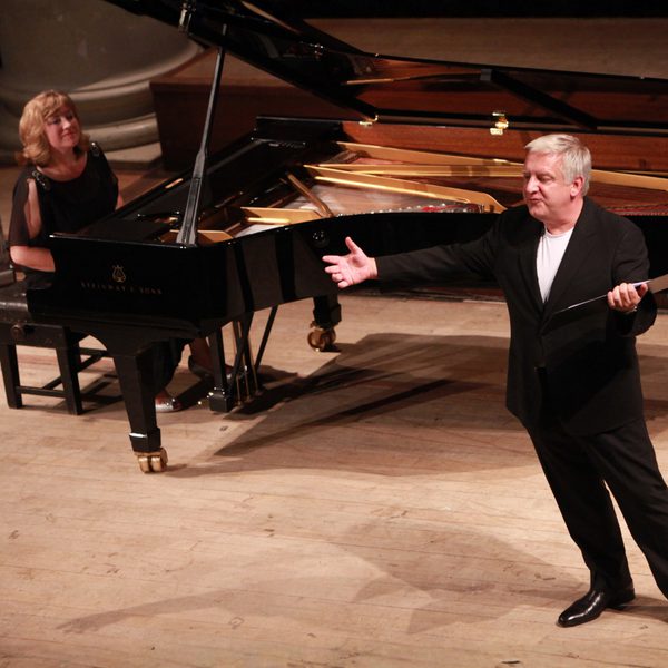 Pianist Lucy Parham and actor Sir Simon Russell Beale performing onstage. Lucy is sat at a piano and Simon is standing and gesturing to the audience.