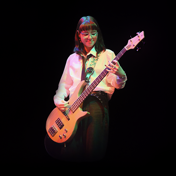 A young person in a shirt and tie playing the electric guitar on stage.