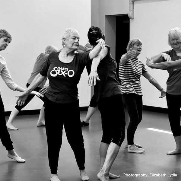 A black and white image of several older people dancing in a rehearsal studio.