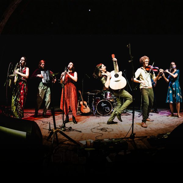Six musicians (the members of Threepenny Bit) performing with various folk instruments on stage.