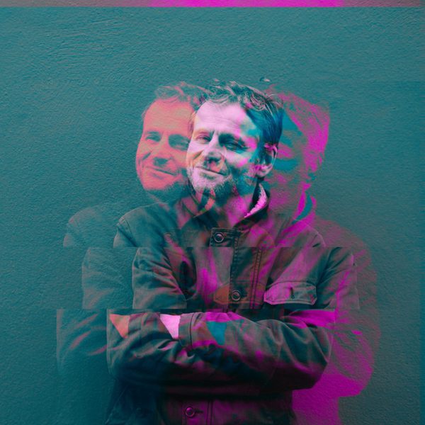 Comedian Will Adamsdale standing with his arms crossed against a blue background. A '3D glasses' effect is on him, with doubles in pink and blue crossing over him.