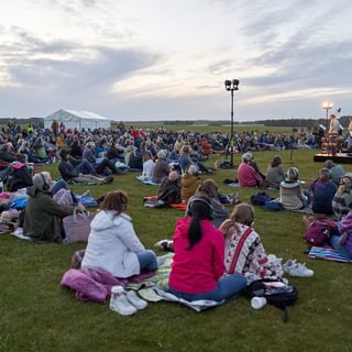 Audience members sat on the ground at Stonehenge watching a performance.