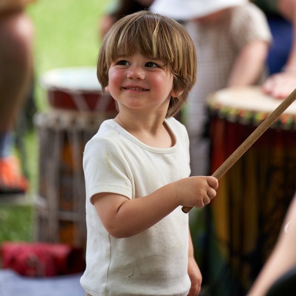 A young boy holding a drumstick and playing music in an outdoor setting.