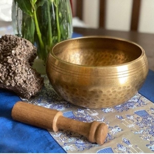 A Tibetan brass singing bowl and stick on a table.