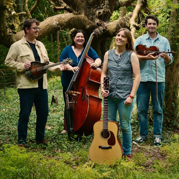 The Charlotte Carrivick Band holding various instruments and smiling in a wooded clearing.