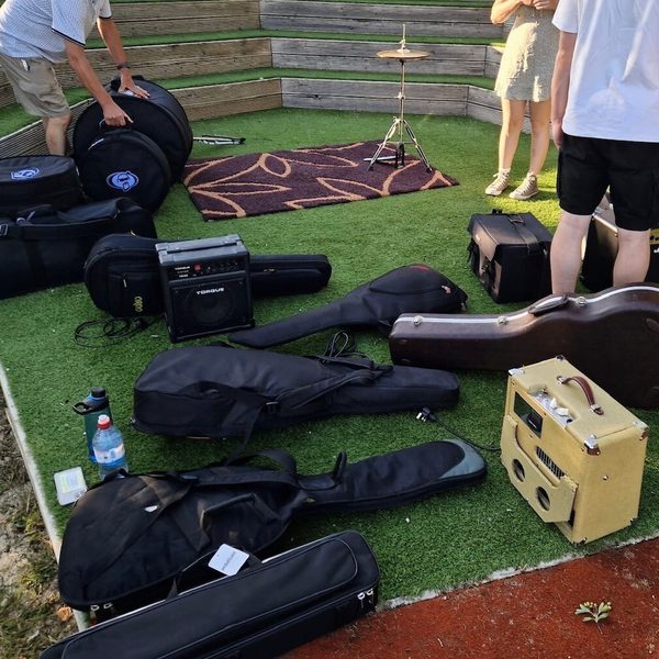 Several instruments in cases laid out on a grass turf. Two young people stand above camera.