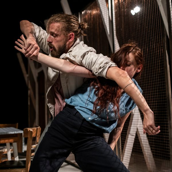 Two dancers dressed in formal wear, 1 male and 1 female, intertwined in a dance.