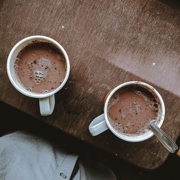 Two mugs of hot chocolate on a wooden board.